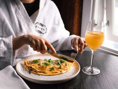 person in bathrobe eating an omelette