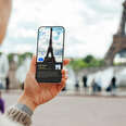 Over the shoulder view of a young person using a virtual tour guide app on their smartphone while travelling in Paris