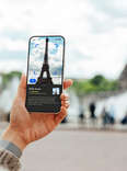 Over the shoulder view of a young person using a virtual tour guide app on their smartphone while travelling in Paris