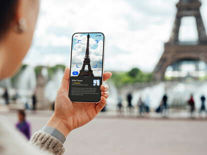Over the shoulder view of a young person using a virtual tour guide app on their smartphone while travelling in Paris