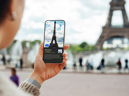 Over the shoulder view of a young person using a virtual tour guide app on their smartphone while travelling in Paris