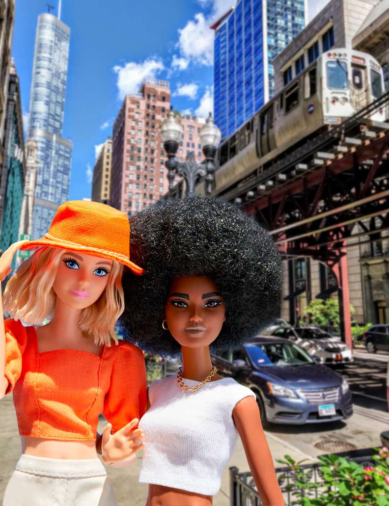 Two Barbie dolls walking on the streets of New York City underneath an above ground subway.