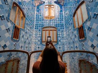 A young woman taking a video of a colorful mosaic wall in Barcelona, Spain.