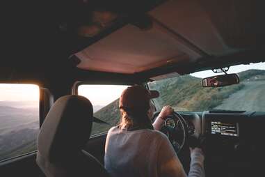 woman driving a car up an elevated dirt road