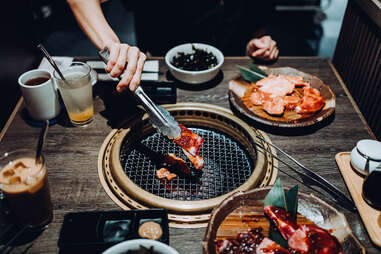 Cropped shot and high angle view of young Asian woman having traditional Japanese style beef barbecue "Yakiniku" in a restaurant and putting raw beef slices over the charcoal grill stove