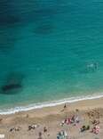An aerial view of the clear blue waters in Nice, France, and beachgoers laying on the sand.