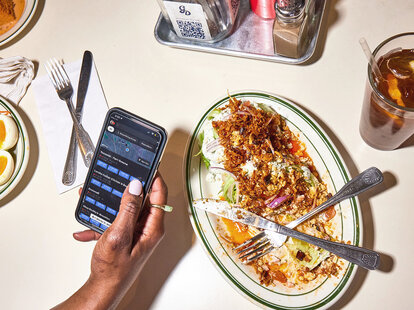 A person using their phone over a finished dinner at a table.