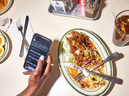 A person using their phone over a finished dinner at a table. 