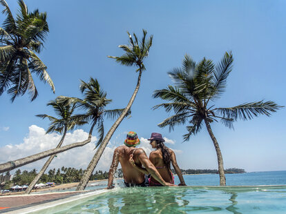 Young people on vacation at the edge of a pool overlooking a tropical scene