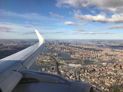An aerial view of New York City from an airplane window, with the plane’s wing in the photo.