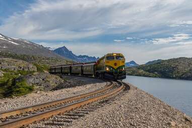 a train on the Alaska Railroad White Pass & Yukon Route by a river and mountains 