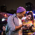 oung friends using mobile phone at festival at night - including a transgender person.