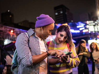 oung friends using mobile phone at festival at night - including a transgender person.