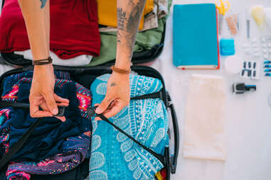 A tattooed person packs clothes and all the necessities for traveling in a suitcase