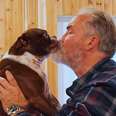 Brown dog being held up by man, kissing dog's snout