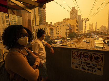 People wear masks as they wait for the tramway to Roosevelt Island, in New York City. The poor air quality caused by wildfire smoke makes the sky appear orange.