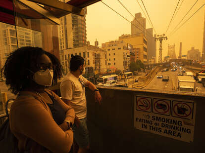 People wear masks as they wait for the tramway to Roosevelt Island, in New York City. The poor air quality caused by wildfire smoke makes the sky appear orange. 