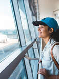 Young woman at the airport, looking out at an airplane. 