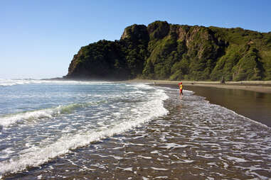 person walking along karekare beach, new zealand