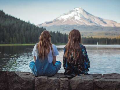 women with long hair sitting by a lake