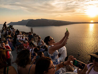 Tourists taking pictures and selfies during sunset in the town of Oia in Santorini