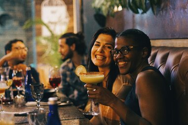Two smiling women holding drinks at a bar in Colombia.