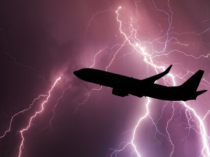 An airplane silhouette on the background of a stormy sky with lightning.