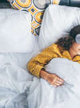 woman laying in bed with eye mask and iphone