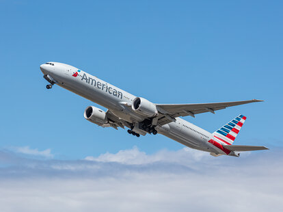 American Airlines, Boeing 777, taking off through the clouds into a bright blue sky.