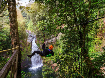 Young man riding on a zip line rope in an extreme adventure jungle