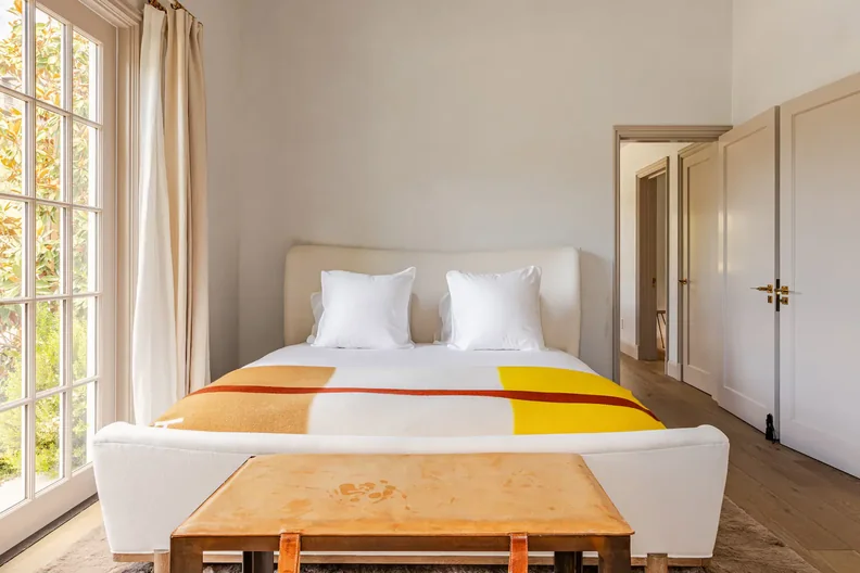 A bedroom with a large white bed and a lot of natural light.