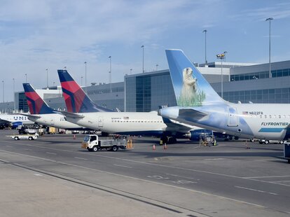 A Frontier Airlines plane (R) sits near other planes at the gate at Denver International Airport