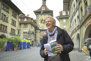 rick steves walking through a european city with a guidebook