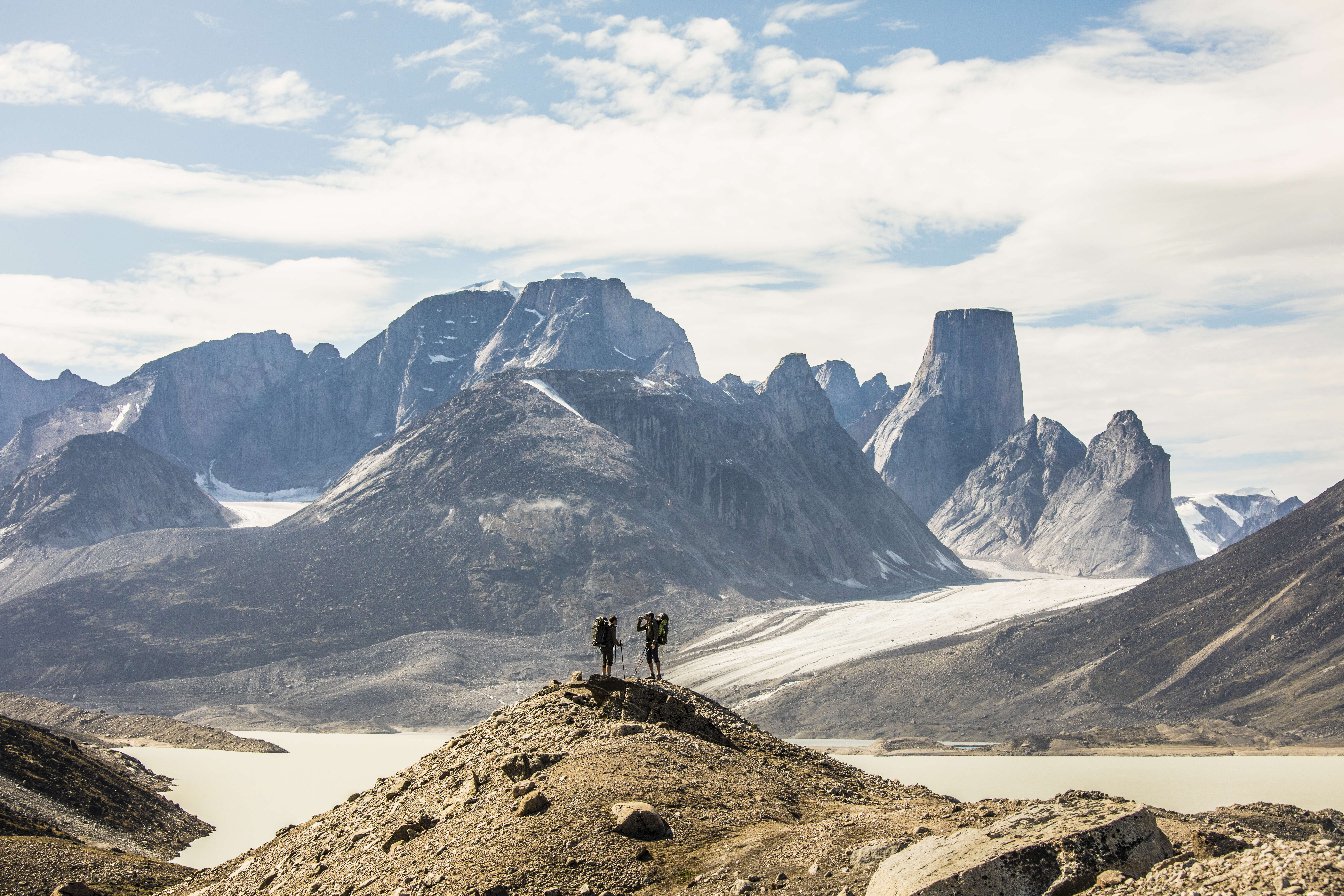 two backpackers standing on distant mountain ridge, nunavut canada