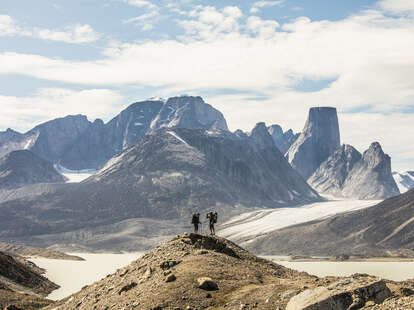 two backpackers standing on distant mountain ridge, nunavut canada