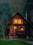 cabin in the woods at twilight next to group of people enjoying campfire