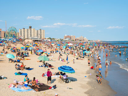 Crowds of people flock to the Coney Island beach and boardwalk on a hot summer weekend.