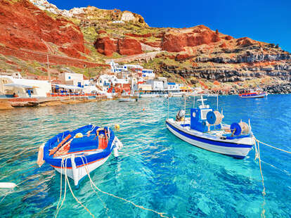 Breathtaking beautiful landscape of two fishing boats anchored to quay in fascinating blue water at the amazing old port panorama in Oia Ia village on Santorini Greek island in Aegean sea.