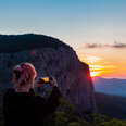 Girl traveler enjoy the nature mountain peak by mobile phone device taking shot the the morning sunrise. Using a smartphone for photography
