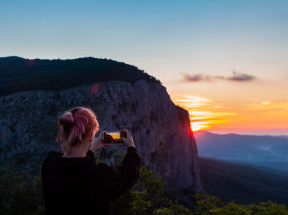 Girl traveler enjoy the nature mountain peak by mobile phone device taking shot the the morning sunrise. Using a smartphone for photography