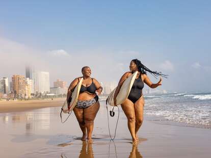 Two women carrying surfboards