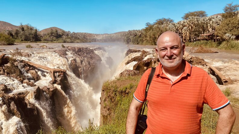 man poses in front of waterfall