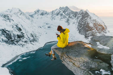 woman uses phone on top of a mountain