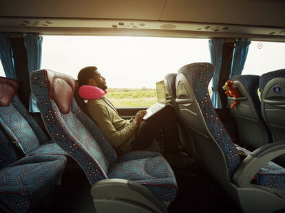 Portrait of smiling man using laptop computer in bus travel.