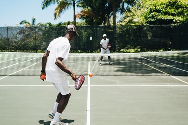 friends playing pickleball at court with palm trees in background