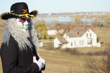 man with face paint and cowboy hat with haunted fort in the distance