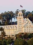 The Fairmont Hotel, in Berkely California. The hotel has the appearance of a castle, with turrets and white walls, amongst trees at sunset. 