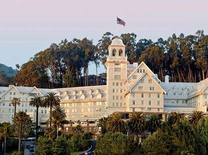 The Fairmont Hotel, in Berkely California. The hotel has the appearance of a castle, with turrets and white walls, amongst trees at sunset.