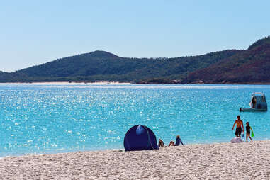 rourists relaxing in front of a tent on the white silica sand beach in whitsunday islands australia