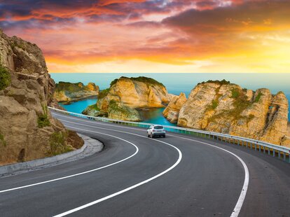 Car driving on mountain road by the sea.